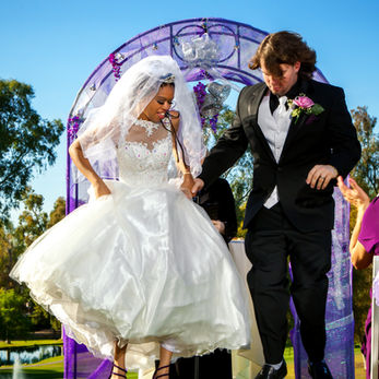 Bride and groom jumping in the air across a traditional style broom that is decorated and laid on the ground