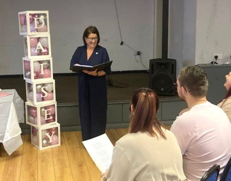 Female Family Celebrant dressed in blue standing beside balloon boxes and in front of guest delivering a naming cermony