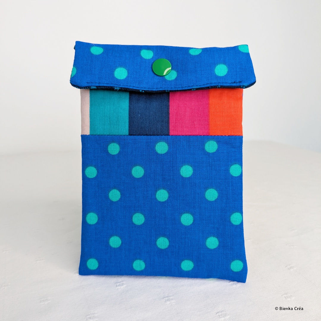Vue d'une pochette bleue à pois verts avec une bande de tissu multicolore fermée par un bouton pression vert