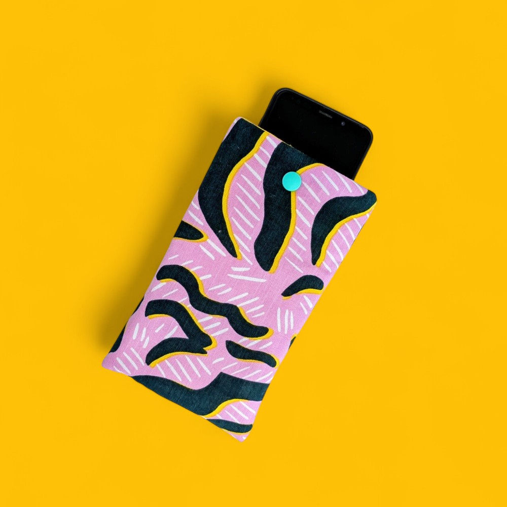 Vue d'un téléphone dans sa pochette molletonnée en coton rose zébré se fermant par un bouton pression vert