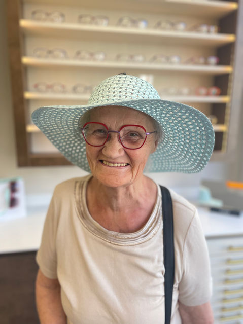 banks opticians client posing new glasses that are a vibrant red whilst wearing a light blue straw hat