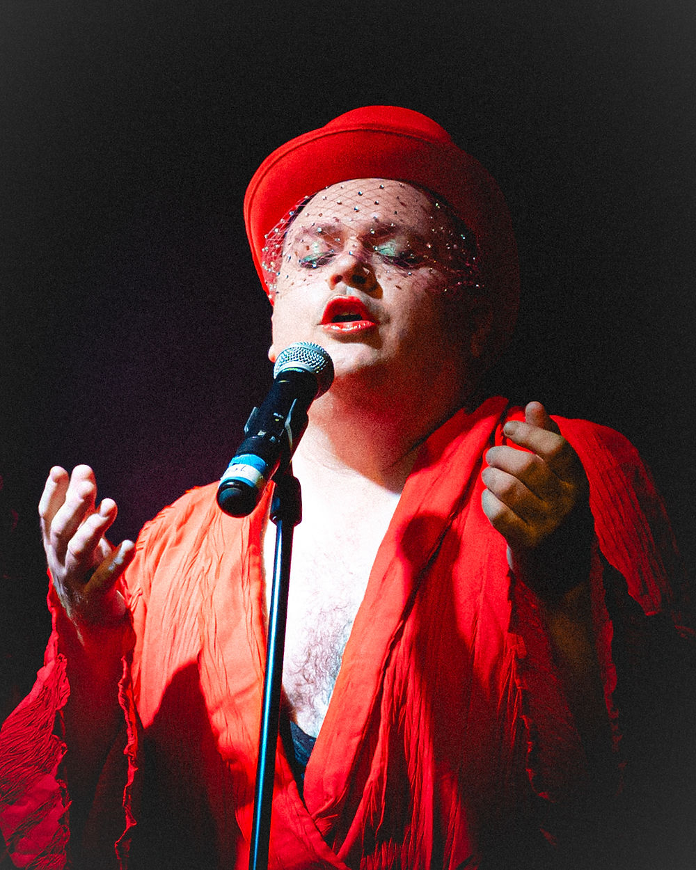 Performer in red hat and robe singing into microphone for events.