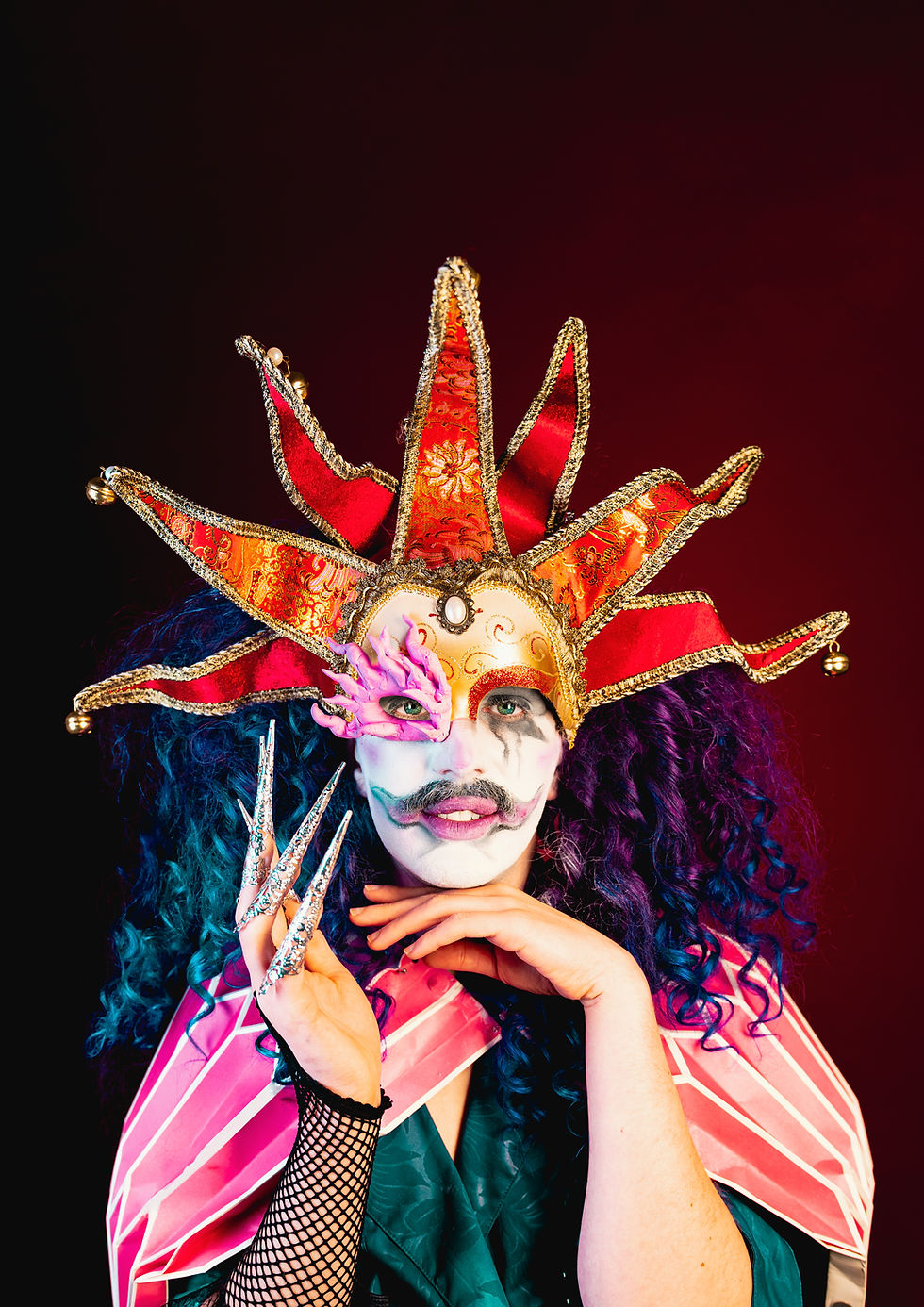 Dramatic performer in intricate jester costume, spiked headpiece, and bold makeup.