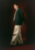 Young man in blazer and wide pants posing dramatically against red backdrop.