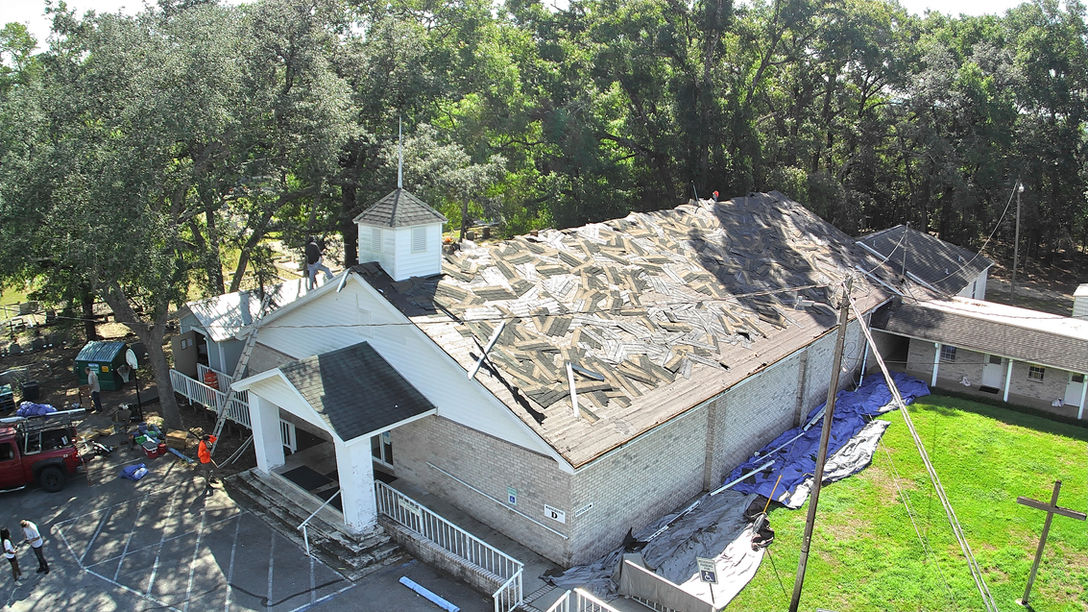 Aerial view of a church roof under renovation with workers removing old shingles, showing progress in the roofing and restoration project.