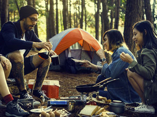 Group of friends cooking breakfast at a forest campsite with a tent in the background, enjoying a relaxed outdoor tent camping experience.