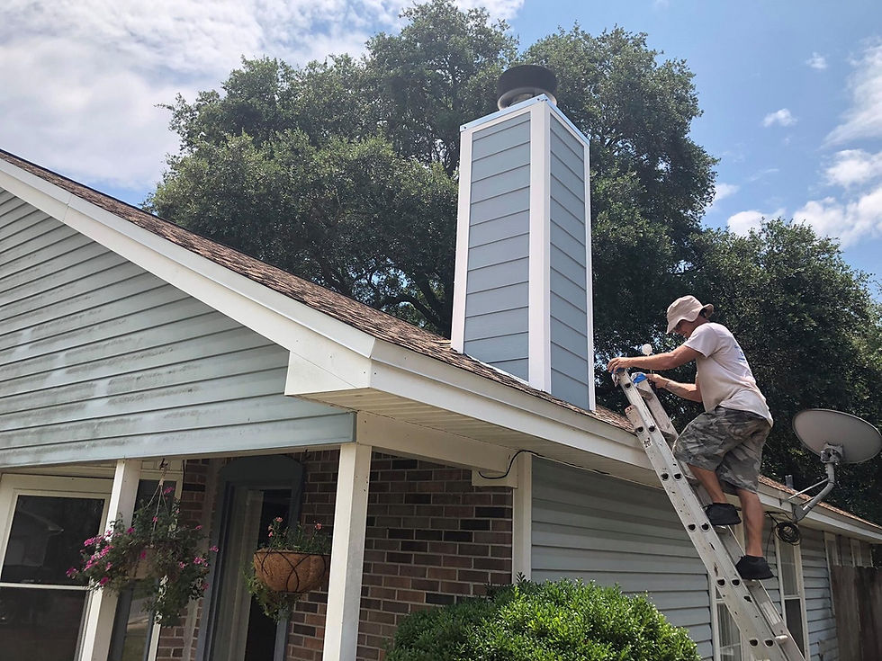 Technician working on a residential roof near the chimney while standing on a ladder outside a single-story home.