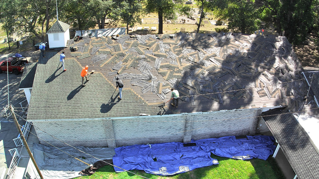 Construction crew working on a large church roof replacement, removing old shingles and preparing the surface for new installation.