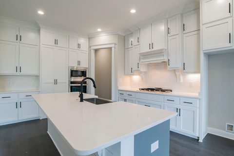 Modern kitchen with white cabinetry, large center island with sink and black faucet, built-in appliances, and recessed lighting.