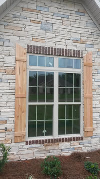 Exterior view of a large window with grid panes, framed by wooden shutters and set in a stone and brick wall façade.