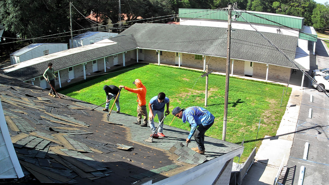 Roofing team removing old shingles and preparing the roof surface for renovation on a large building with an open courtyard.