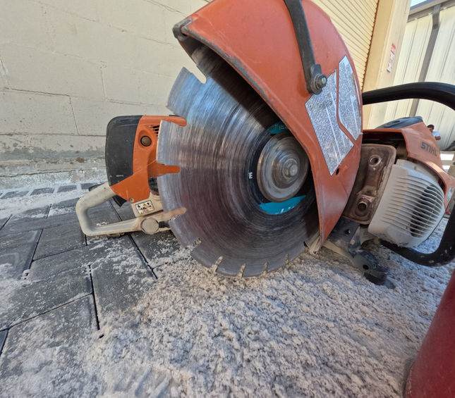 Close-up of a concrete saw cutting paver stones during a construction project, showing precision masonry work and attention to detail.