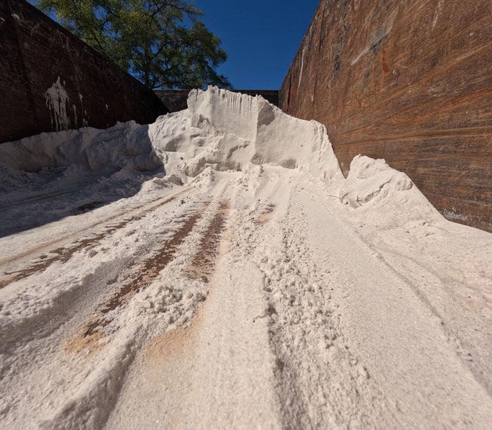 Large pile of white construction sand or fill material loaded inside a dump trailer under clear blue skies, ready for site preparation or grading work.