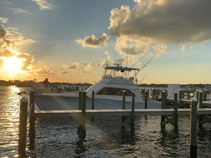 Luxury charter boat docked in Destin, Florida marina at sunset with golden sky, calm water, and scenic coastal views.