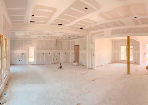 Interior view of a home under construction with drywall installed and unfinished flooring, showing open layout and multiple doorways.