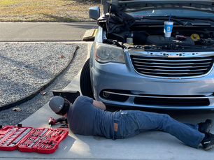 Mobile mechanic performing roadside car repair on a vehicle with the hood open in a Fort Walton Beach residential area, using professional tools laid out beside the car.