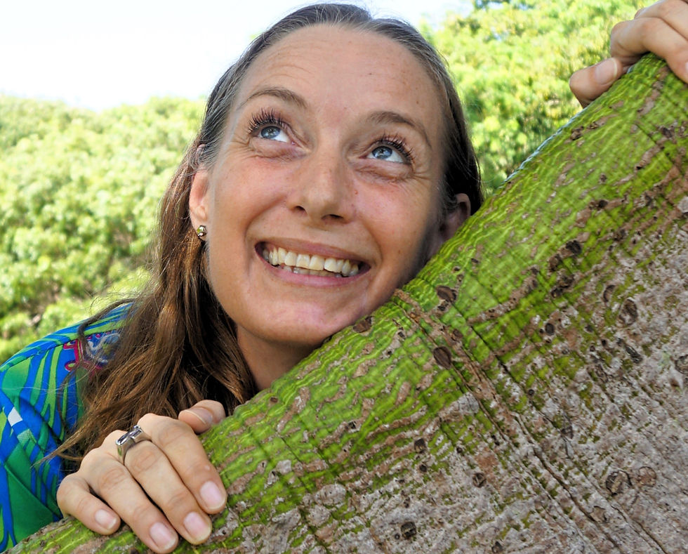 Nat smiling and looking upward, leaning on a tree with textured bark. Lush greenery in the background. Cheerful and bright mood.
