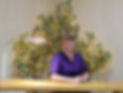 An Image of Michelle Pearce, the Owner of NextGen sitting at a table with a tree with yellow lights on it behind her.