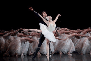 Male and female lead ballet dancers in pose in front of several other dancers in white costume