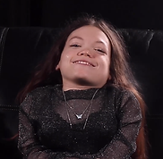 Singer-songwriter Gracie Moyes smiling while seated on a black sofa in a studio setting.