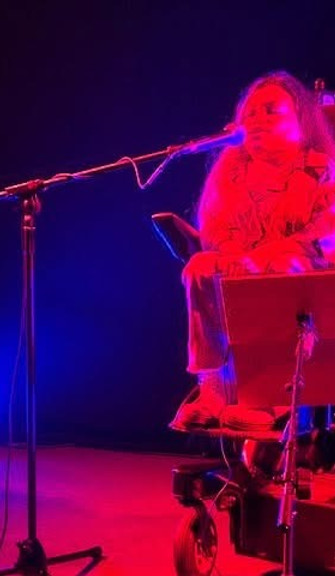 Gracie Moyes performing live music on stage with microphone and dramatic lighting. 