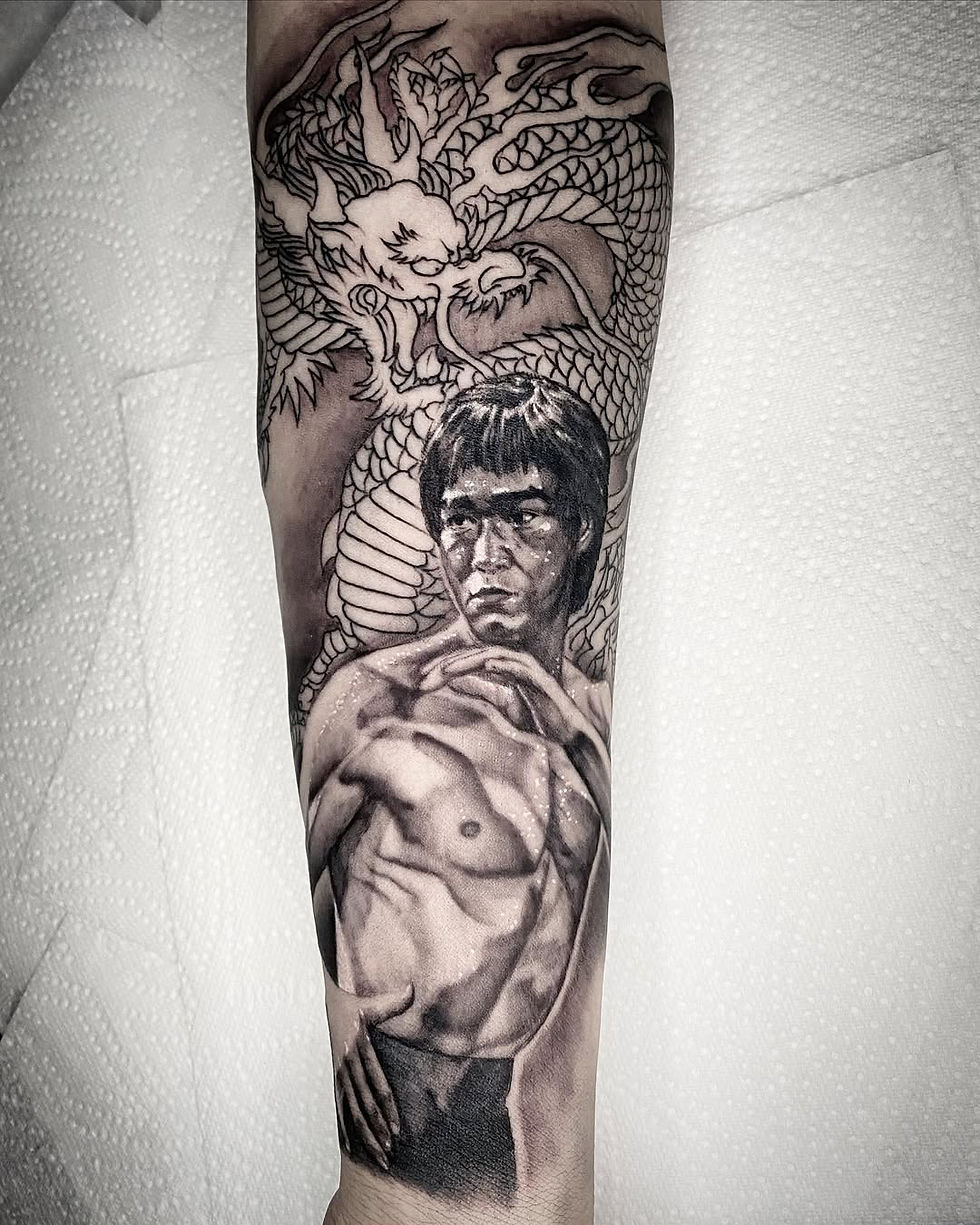 Tattoo of Bruce Lee a martial artist and dragon on an arm. The detailed grayscale design depicts strength and intensity. Background is white paper.