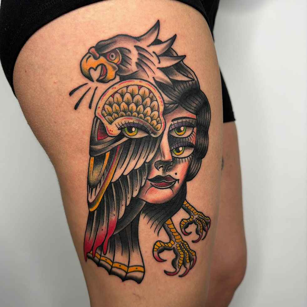 Tattoo on thigh depicting a stylized woman's face merged with an eagle, featuring vibrant reds and yellows, creating an intense look.