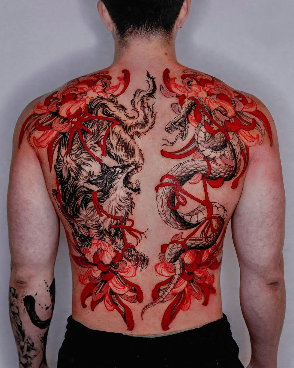 Man's back with detailed tattoos: black wolf and snake facing each other amid vivid red floral patterns, conveying intensity and artistry.
