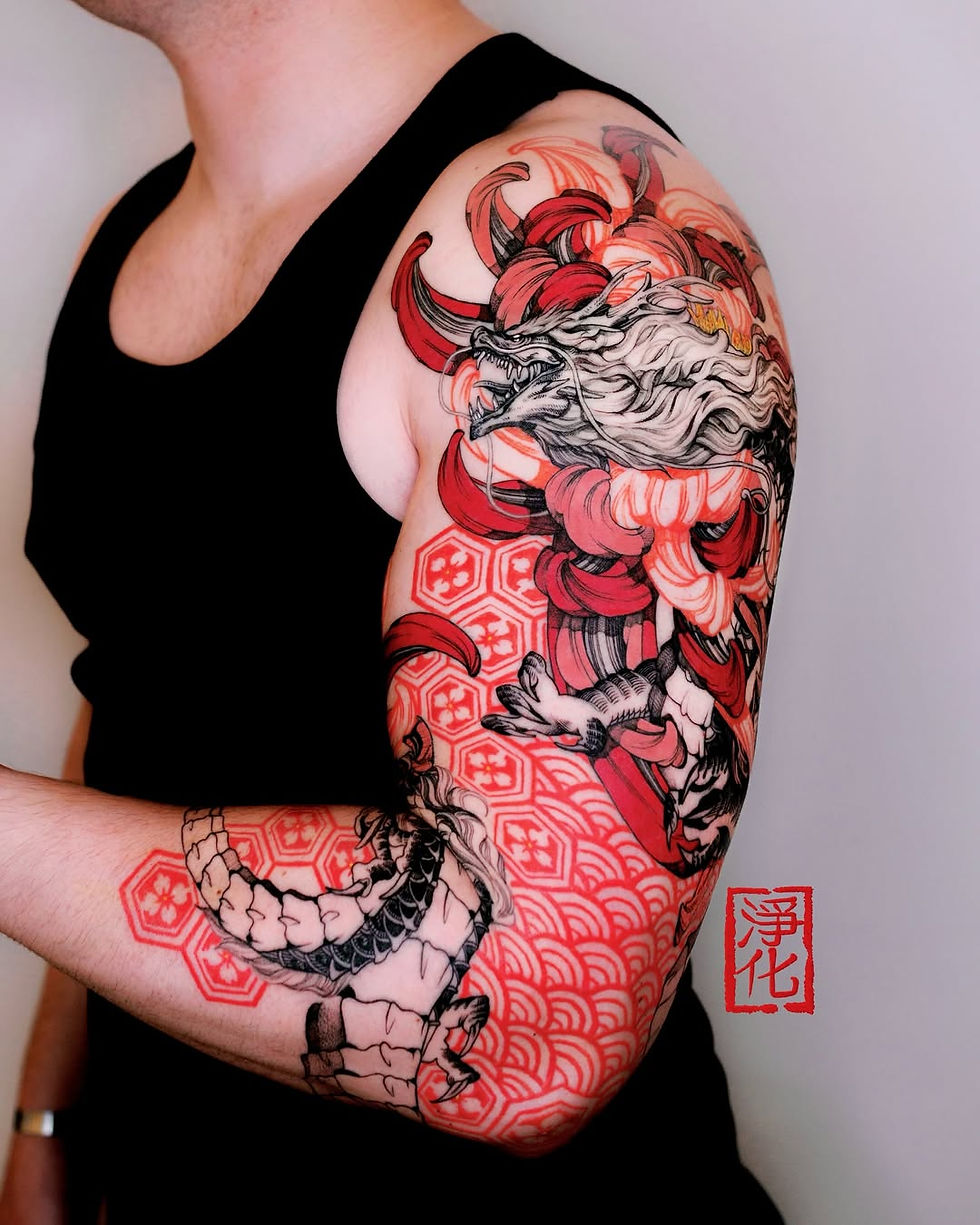 Man in black tank top with a colorful dragon tattoo on his arm. Red, black patterns and Japanese text, set against a plain background.