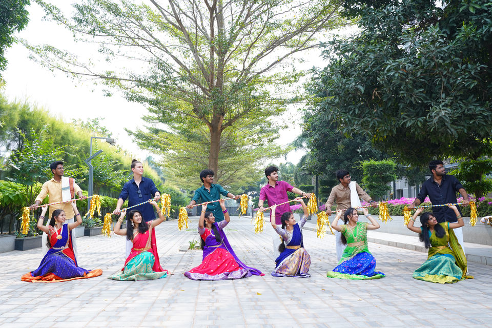 Students performing traditional dance wearing colorful clothes near a large tree.