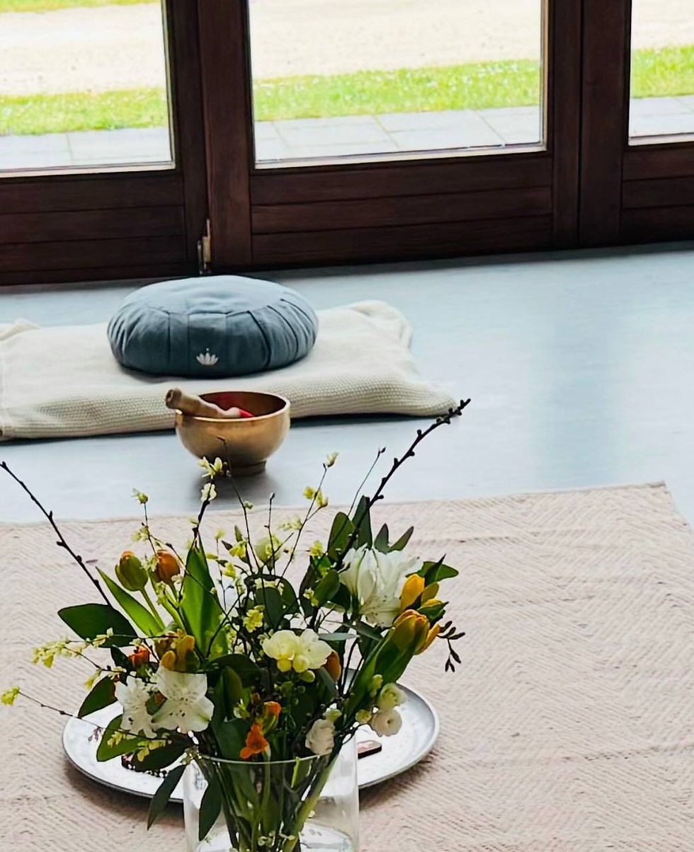 Ein Mediationsraum mit Sitzkisssen, Klangschale und Blumen.