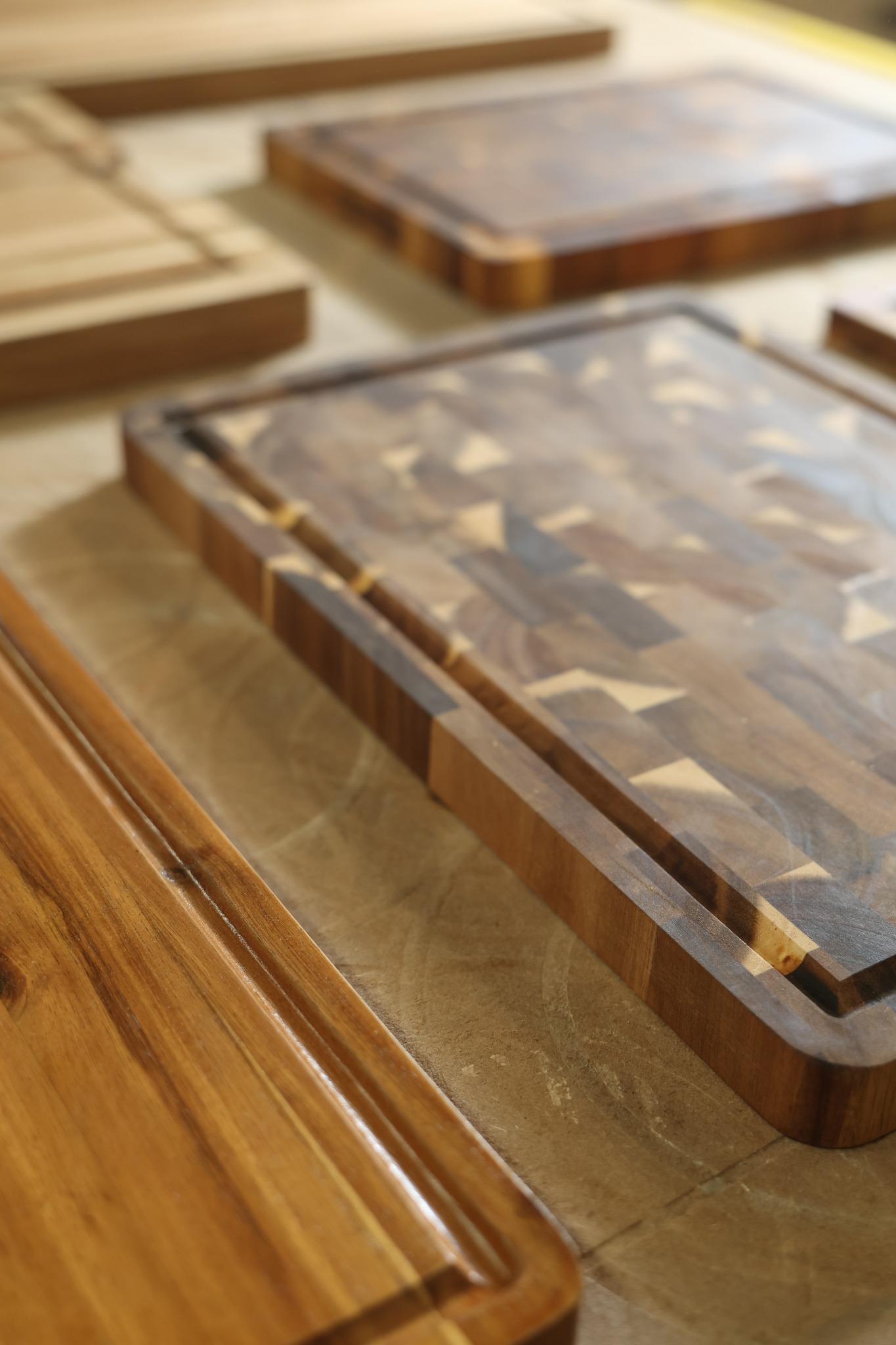 Close-up of an end-grain cutting board edge and juice groove beside straight-grain boards in our Vietnam workshop