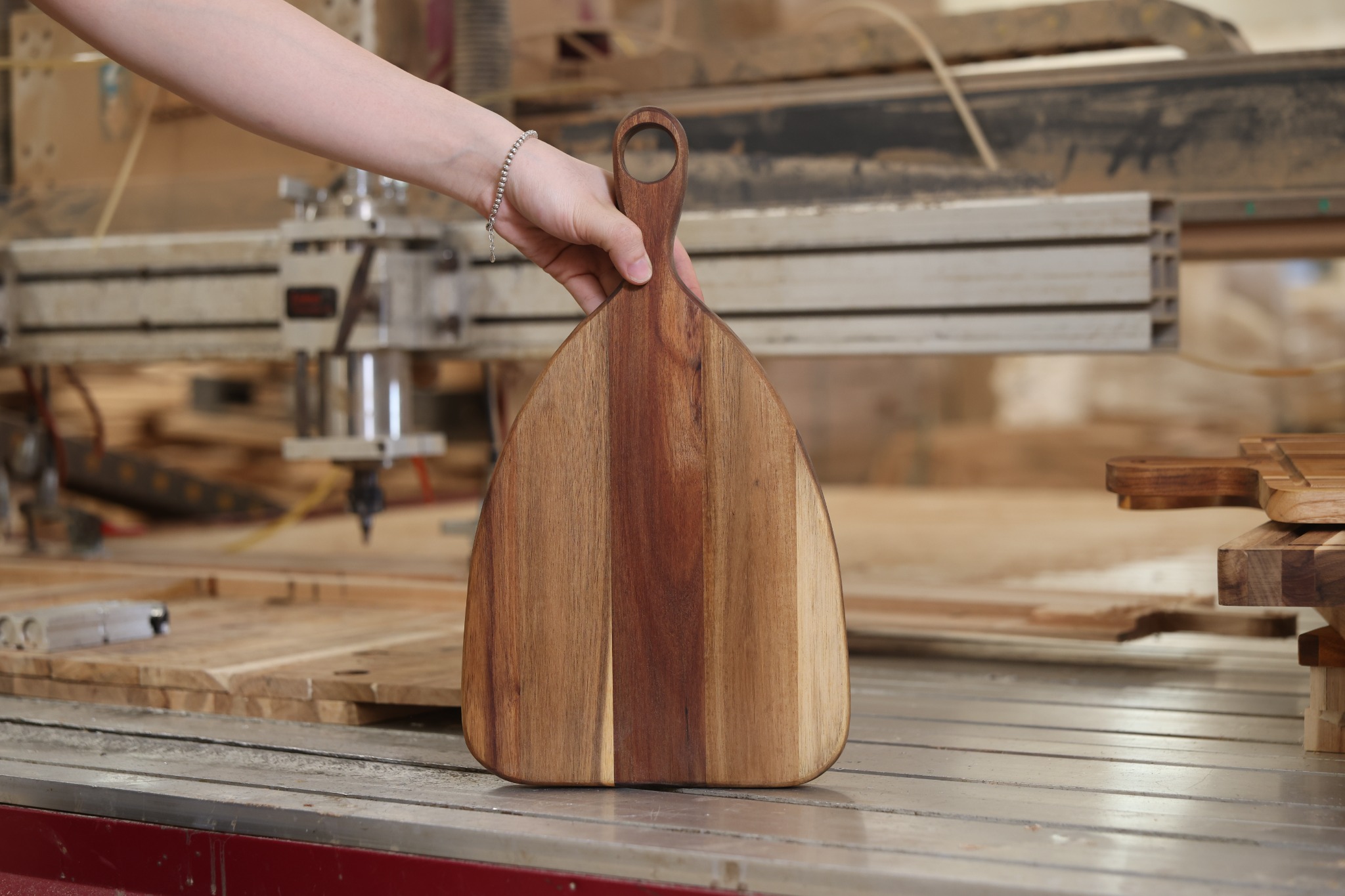 Teak paddle cutting board with a curved profile, natural grain and a large hanging hole