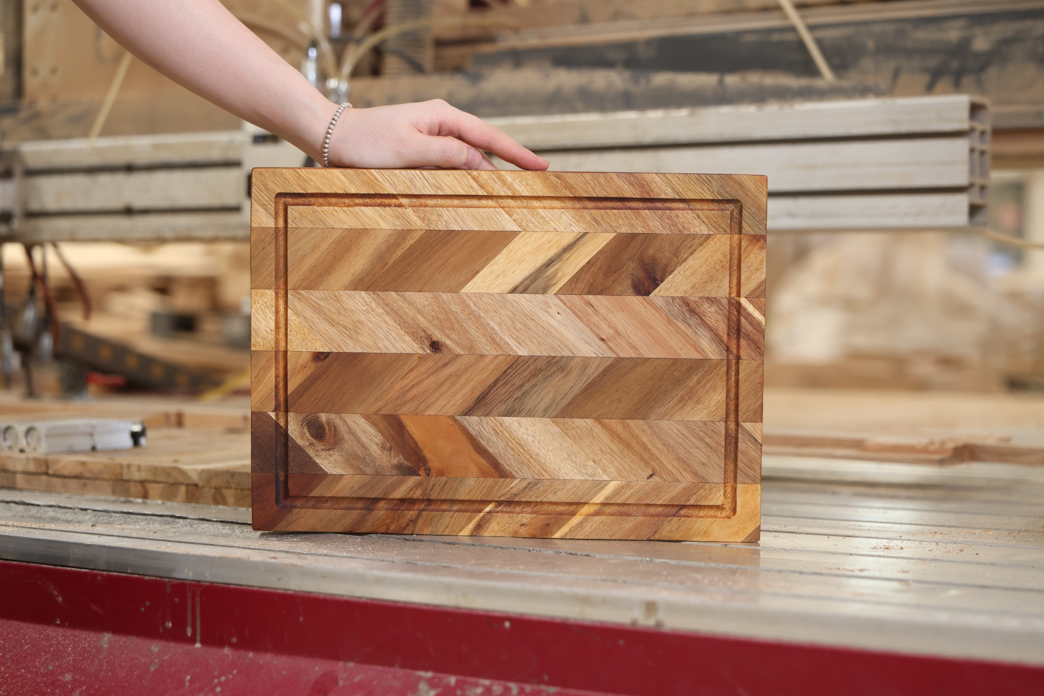 Chevron wooden cutting board with a continuous perimeter juice groove held upright on a factory worktable