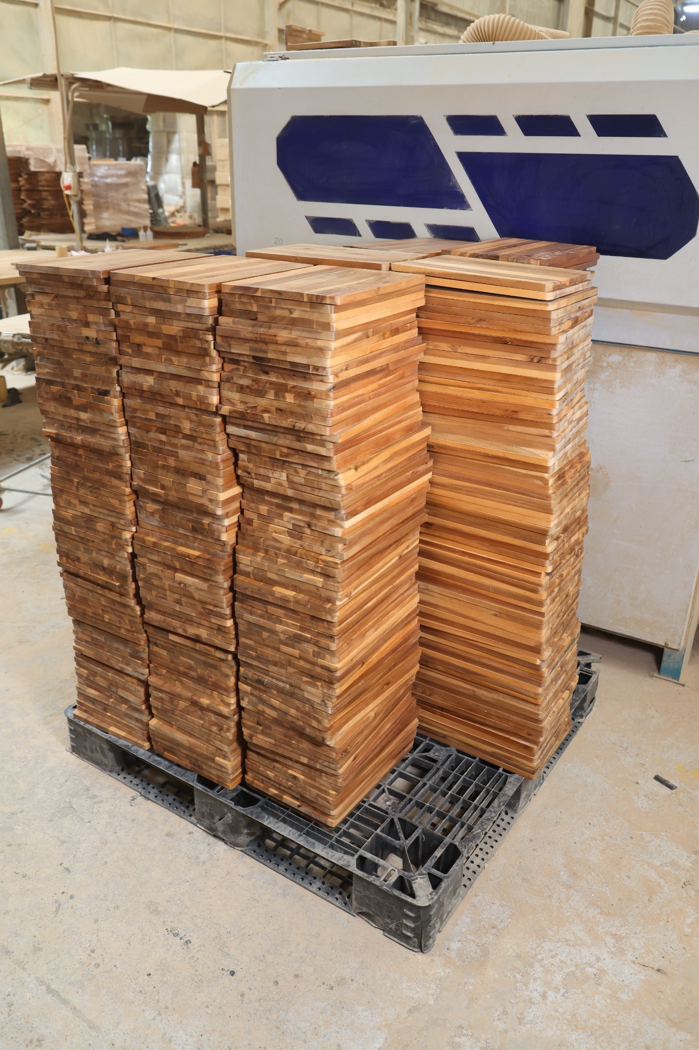 Stacks of rectangular acacia cutting boards beside factory machinery in Vietnam