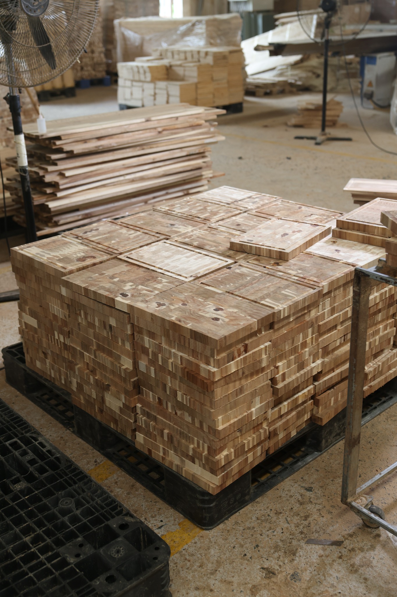 Unfinished acacia cutting boards with routed juice grooves stacked during factory production in Vietnam