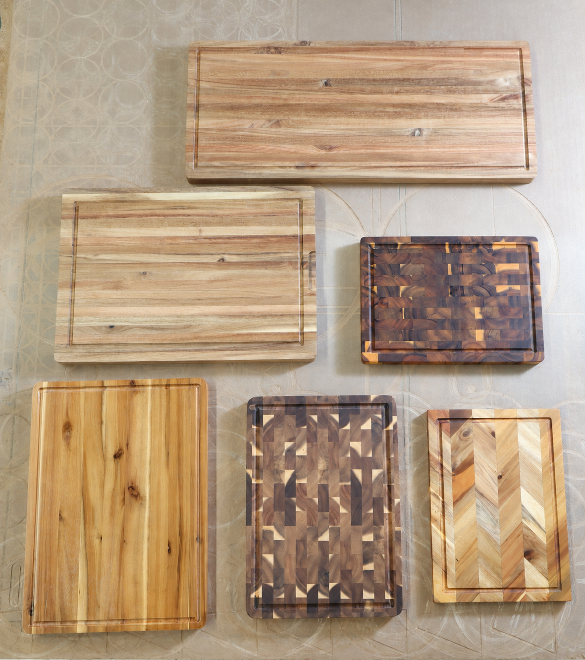 Overhead view of six wooden cutting board designs; the largest top board has a continuous perimeter juice groove
