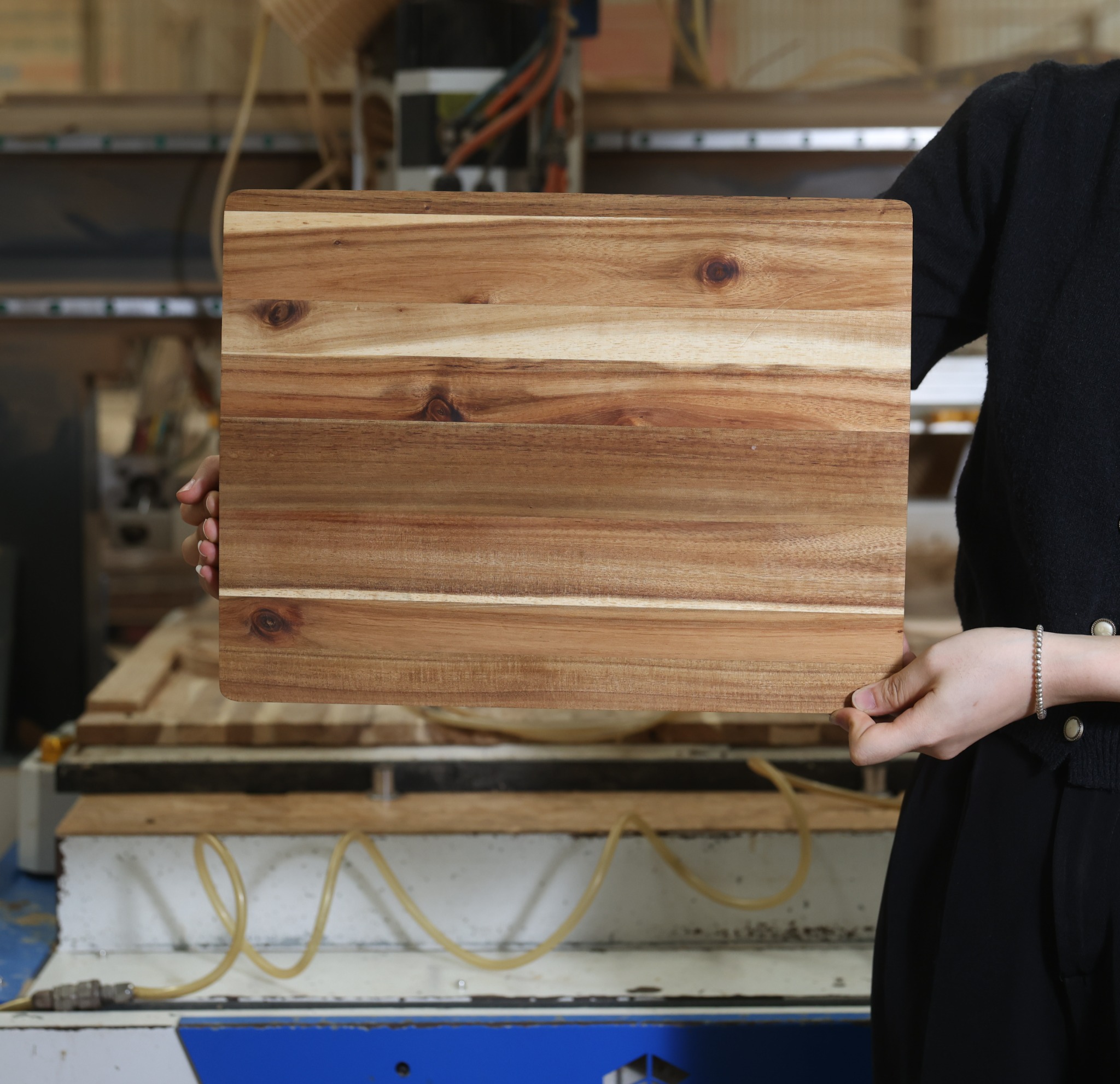 Factory team member holding a rectangular acacia cutting board with rounded corners and natural grain in Vietnam