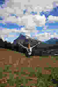 Leanne sitting on hill with mountains in the background and blue skies with white fluffy clouds