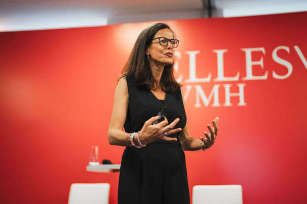 Female speaker presenting at stage in front of red backdrop