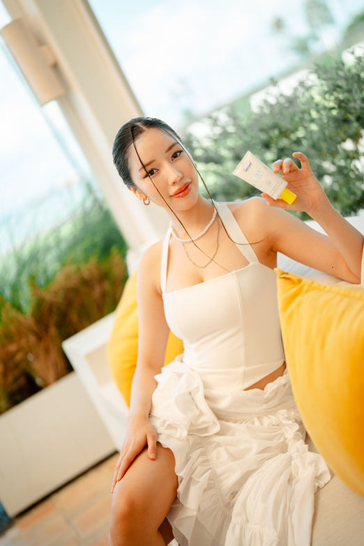 Guest posing with Supergoop product on yellow pillow backdrop