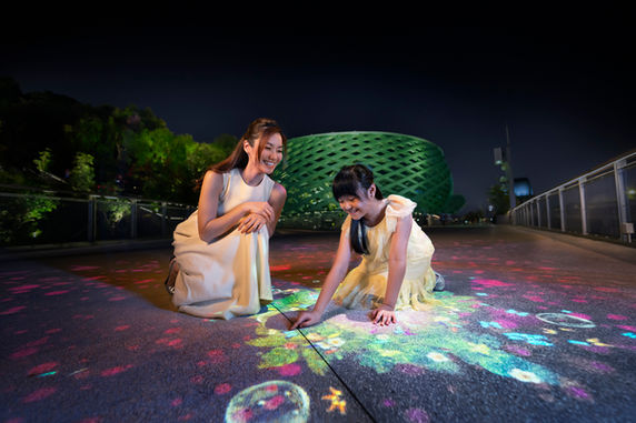 Nighttime shot of women creating glowing artwork on interactive light-up floor installation