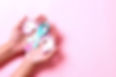 Teal awareness ribbon with cervix shape on palms hand over pink background with copy space