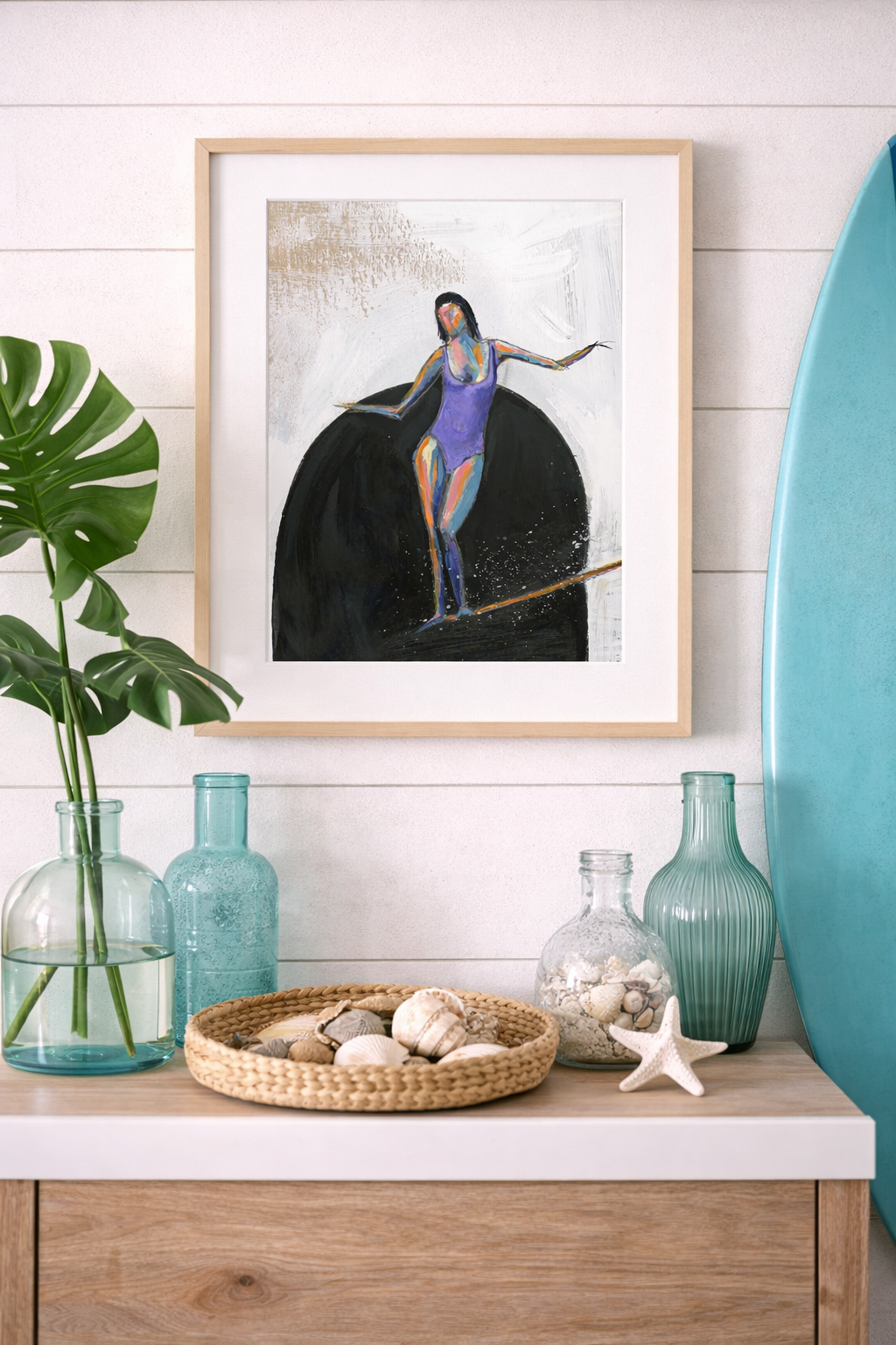 8.5x11 framed surfer girl painting with white mat styled in a modern beach house with sea glass vases, monstera leaves, shell