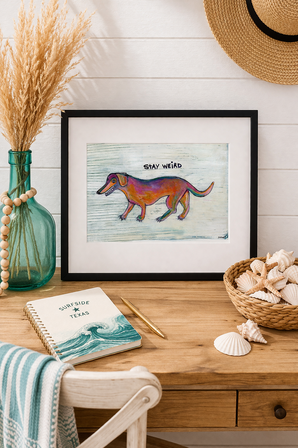 Stay Weird dachshund mini print in a black 8x10 frame with white mat, styled on a warm wood coastal desk with a turquoise gla