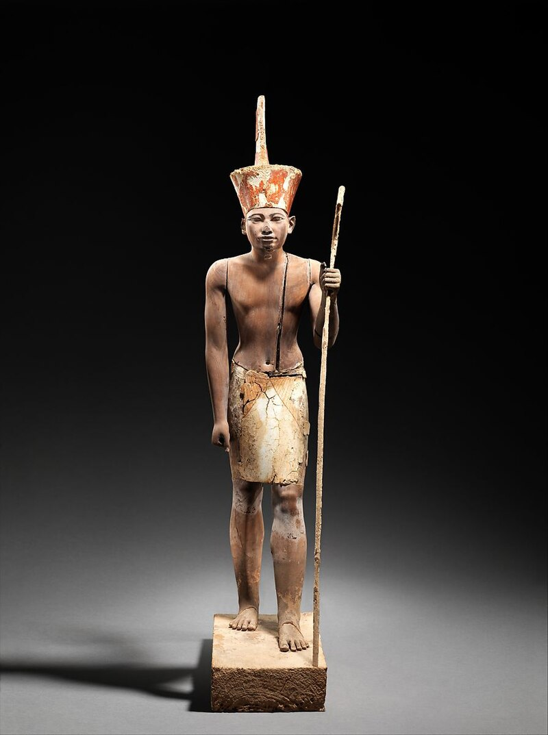 A figure wearing the red crown of Lower Egypt, most probably Amenemhat II or Senwosret II. It functioned as a divine guardian for the imiut; the divine kilt suggests that the statuette was not merely a representation of the living ruler.