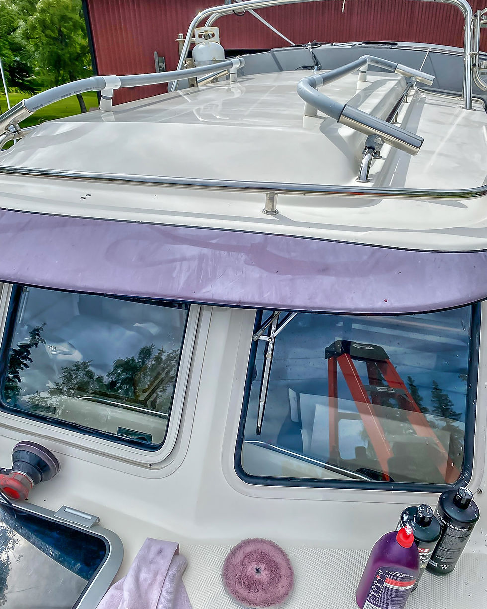 Boat deck being cleaned, polish and buffer on deck. Green trees reflected in windows. Red ladder visible inside. Calm outdoor setting.