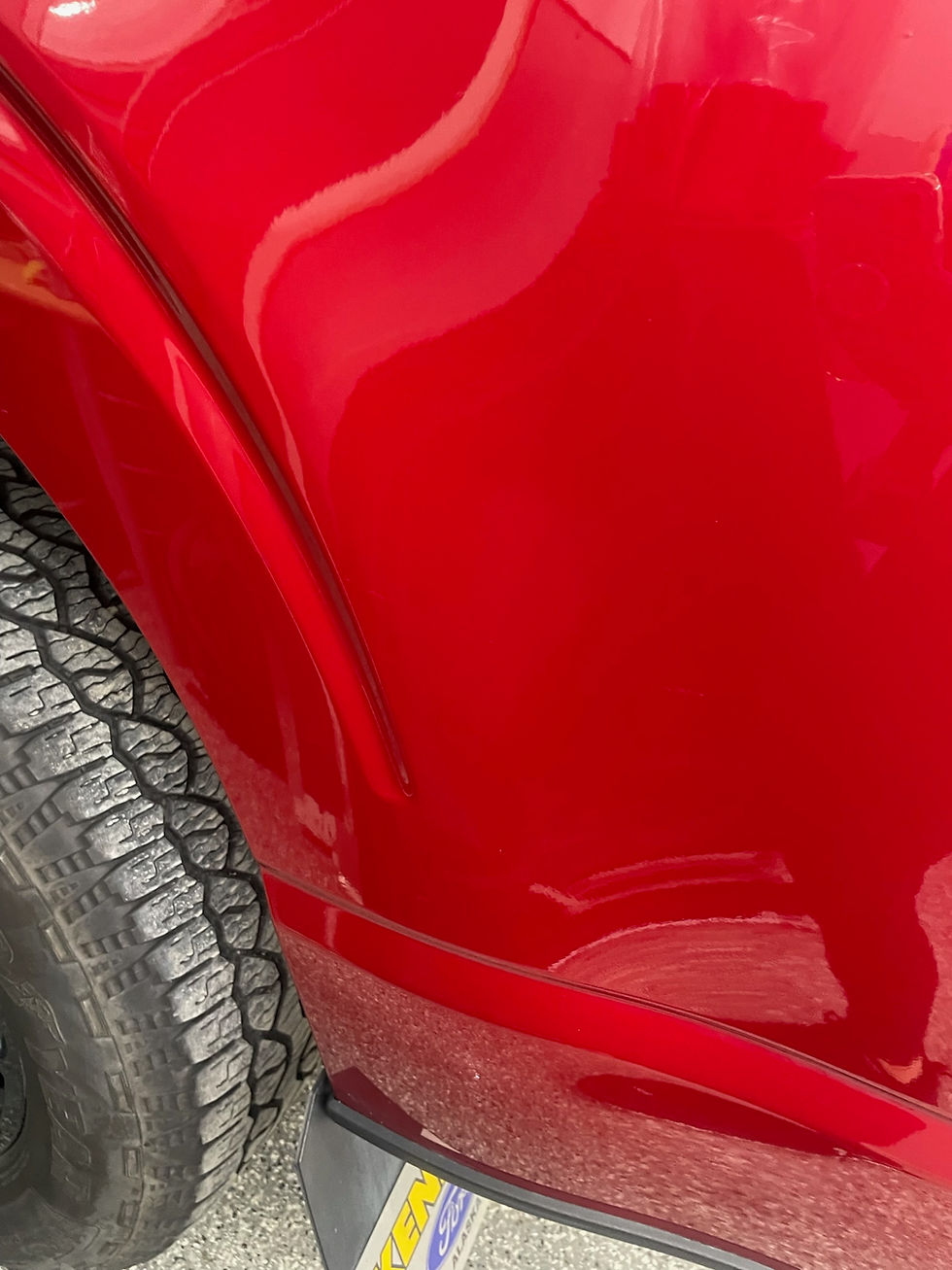 Close-up of a shiny red car fender with a textured tire. Reflection in the paint and part of a license plate with faded text visible.