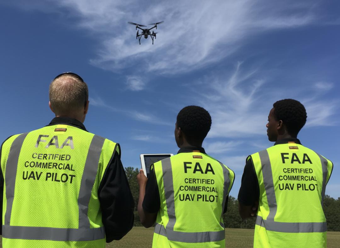 Three FAA Certified Commercial UAV Pilots observe a drone in the bright sky.