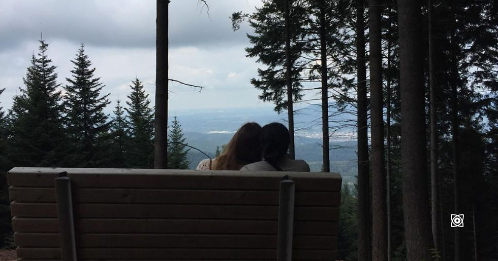 Couple resting on a wooden bench up a hill, gazing at a cloudy mountain valley view.